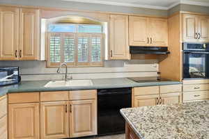 Kitchen featuring light brown cabinets, black appliances, under cabinet range hood, ornamental molding, and tasteful backsplash