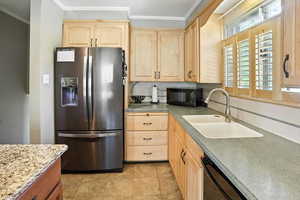 Kitchen featuring light brown cabinetry, black appliances, tasteful backsplash, and ornamental molding
