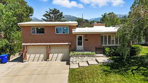 Tri-level home featuring a garage, concrete driveway, brick siding, a mountain view, and a front yard