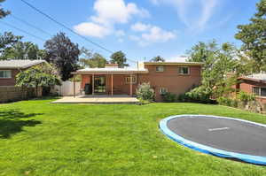 Back of property with a trampoline, a patio area, brick siding, and a chimney