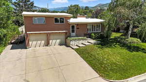 Split level home with brick siding, an attached garage, concrete driveway, and a front lawn
