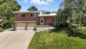 Tri-level home with an attached garage, brick siding, concrete driveway, a front lawn, and a chimney