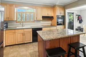 Kitchen featuring crown molding, light brown cabinetry, black appliances, light stone counters, and a breakfast bar