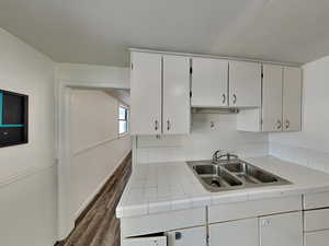Kitchen with dark wood-style flooring, tile countertops, and white cabinets