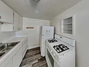 Kitchen with white range with gas stovetop, dark wood-style floors, white cabinets, and light countertops