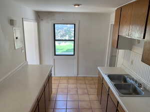 Kitchen featuring light tile patterned floors, electric panel, light countertops, and brown cabinets