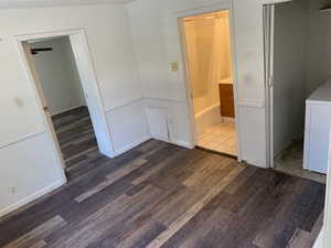 Unfurnished bedroom with a wainscoted wall, wood finished floors, separate washer and dryer, connected bathroom, and a decorative wall