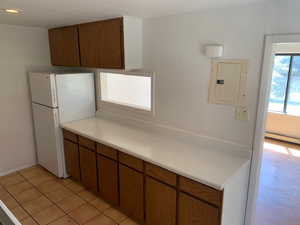 Kitchen featuring freestanding refrigerator, electric panel, light countertops, light tile patterned flooring, and brown cabinets