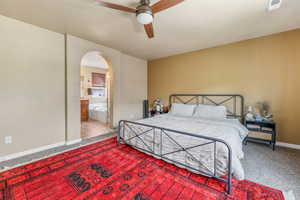 Bedroom featuring carpet floors, arched walkways, ensuite bathroom, and a ceiling fan