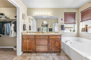 Bathroom with a garden tub, a shower stall, double vanity, stone finish flooring, and a spacious closet