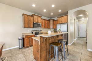 Kitchen with arched walkways, light countertops, appliances with stainless steel finishes, a kitchen breakfast bar, and light tile patterned floors