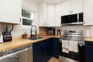 Kitchen with butcher block counters, stainless steel appliances, white cabinets, and blue cabinets