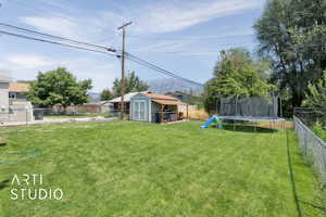 Fenced backyard featuring a trampoline and a shed