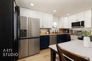 Kitchen with appliances with stainless steel finishes, light wood-style flooring, recessed lighting, a textured ceiling, and white cabinetry