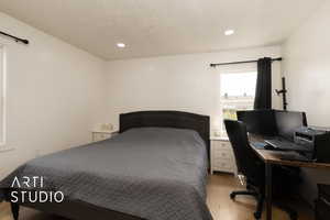Bedroom featuring light wood finished floors, a textured ceiling, an office area, and recessed lighting