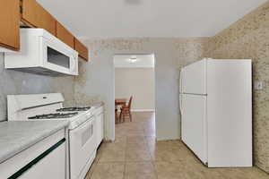 Kitchen featuring white appliances, light countertops, light tile patterned floors, brown cabinets, and wallpapered walls
