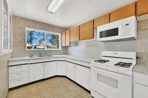 Kitchen featuring white appliances, light countertops, light tile patterned floors, and decorative backsplash