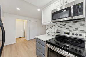 Kitchen with appliances with stainless steel finishes, backsplash, recessed lighting, white cabinetry, and light wood-type flooring