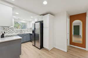 Kitchen featuring stainless steel appliances, light wood-type flooring, decorative backsplash, arched walkways, and white cabinets