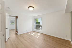 Spare room with healthy amount of natural light, light wood-type flooring, and a textured ceiling