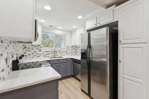 Kitchen with appliances with stainless steel finishes, gray cabinets, light wood-style floors, white cabinetry, and decorative backsplash