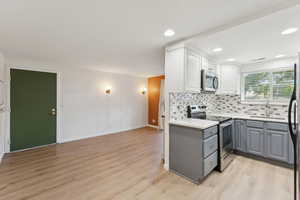 Kitchen featuring gray cabinets, stainless steel appliances, tasteful backsplash, white cabinetry, and light countertops