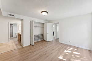 Unfurnished bedroom featuring a textured ceiling, light wood-style floors, a closet, and ensuite bath