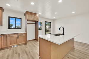 Kitchen with healthy amount of natural light, recessed lighting, light wood-type flooring, light countertops, and a center island with sink