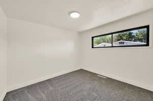 Unfurnished room with dark colored carpet and a textured ceiling