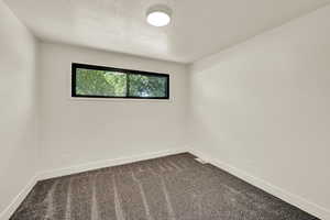 Empty room with dark colored carpet and a textured ceiling