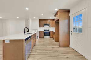 Kitchen featuring appliances with stainless steel finishes, light wood finished floors, brown cabinetry, recessed lighting, and light countertops