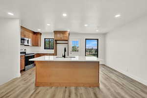 Kitchen with appliances with stainless steel finishes, a kitchen island with sink, recessed lighting, light countertops, and light wood finished floors