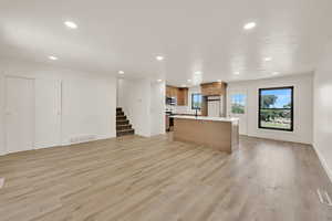 Kitchen featuring open floor plan, brown cabinets, recessed lighting, a center island with sink, and light wood-style flooring