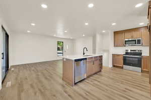 Kitchen featuring appliances with stainless steel finishes, recessed lighting, light wood-type flooring, light countertops, and open floor plan