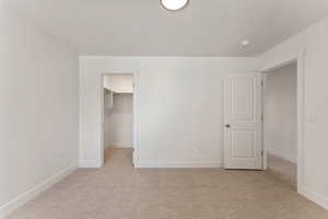 Unfurnished bedroom with light carpet, a spacious closet, and a textured ceiling