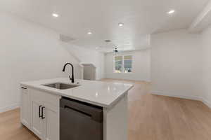 Kitchen with stainless steel dishwasher, light wood-type flooring, white cabinets, a kitchen island with sink, and light stone countertops