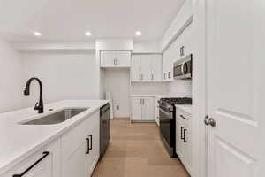 Kitchen with stainless steel appliances, light wood-type flooring, white cabinets, light stone counters, and recessed lighting