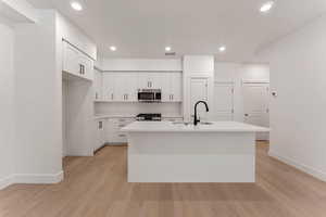 Kitchen featuring white cabinets, a center island with sink, appliances with stainless steel finishes, recessed lighting, and light countertops