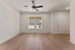 Empty room featuring light wood-type flooring, a ceiling fan, a textured ceiling, and recessed lighting
