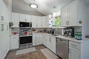 Kitchen featuring lofted ceiling, stainless steel appliances, a textured ceiling, white cabinets, and backsplash