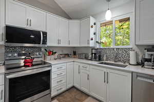 Kitchen with appliances with stainless steel finishes, a textured ceiling, vaulted ceiling, light countertops, and white cabinetry
