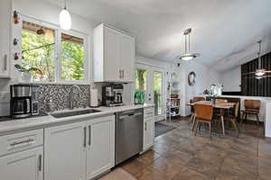 Kitchen with lofted ceiling, a textured ceiling, stainless steel dishwasher, light countertops, and decorative light fixtures