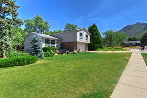Split level home with brick siding, an attached garage, a front yard, and driveway