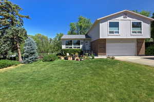 Tri-level home featuring brick siding, a garage, a front yard, and driveway