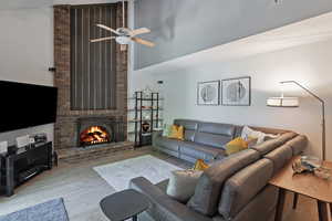 Living room with a high ceiling, wood finished floors, a fireplace, and a ceiling fan