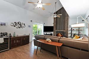 Living area with a fireplace, wood finished floors, wine cooler, high vaulted ceiling, and ceiling fan