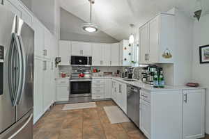 Kitchen featuring lofted ceiling, stainless steel appliances, decorative backsplash, white cabinetry, and a textured ceiling