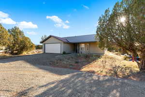 Single story home featuring gravel driveway, an attached garage, and a metal roof
