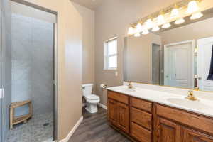 Full bathroom featuring double vanity, wood finished floors, and a tile shower