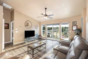 Living room featuring lofted ceiling, a ceiling fan, a textured ceiling, and wood finished floors